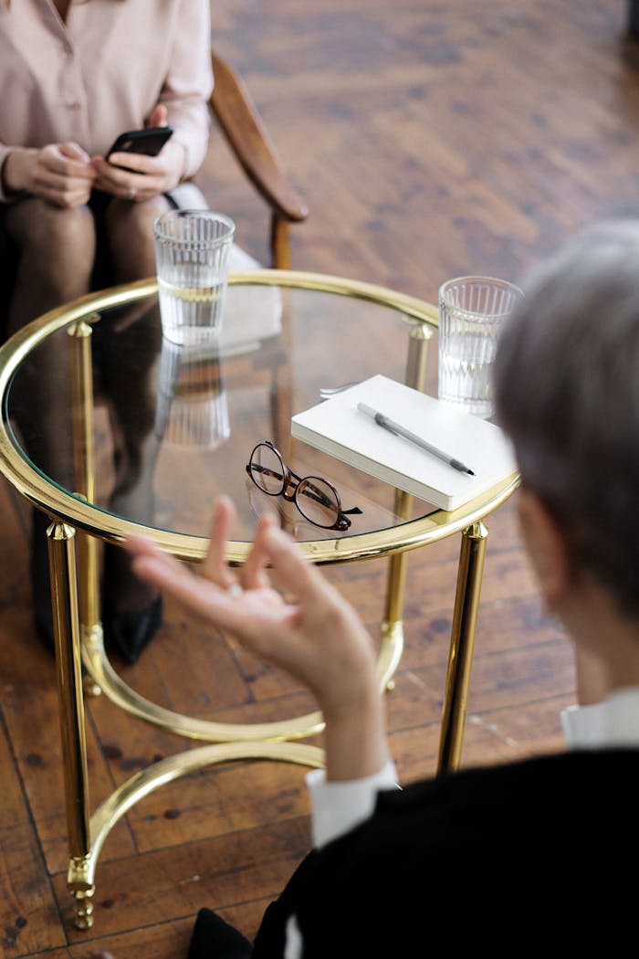Services-03 Two adults engaged in a therapy session, seated at a glass table with notebooks and water glasses.